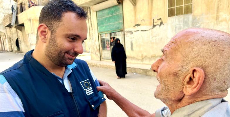 Young male EU aid worker assists older gentleman. 